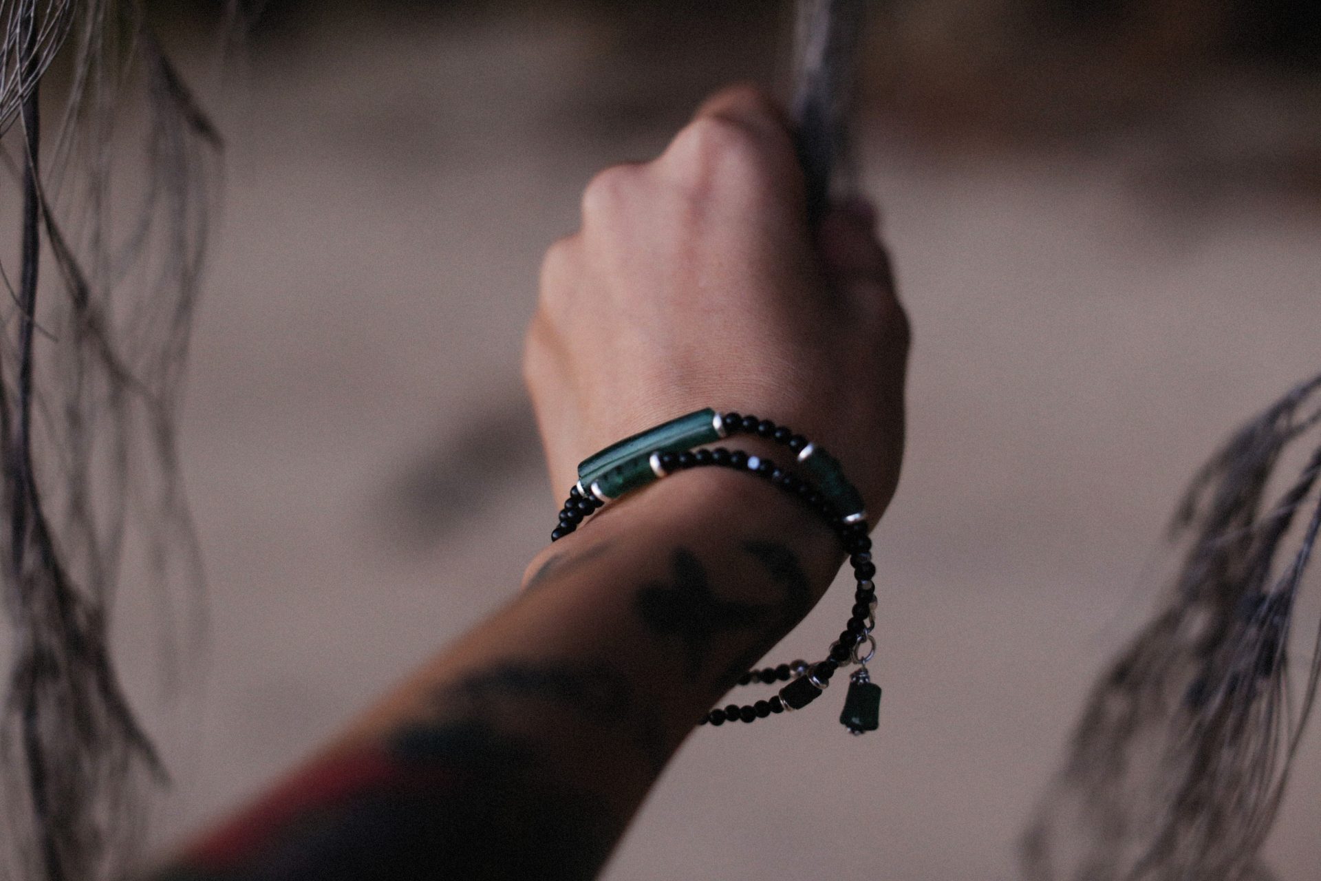 A close-up of a tattooed arm wearing stylish beaded bracelets outdoors.