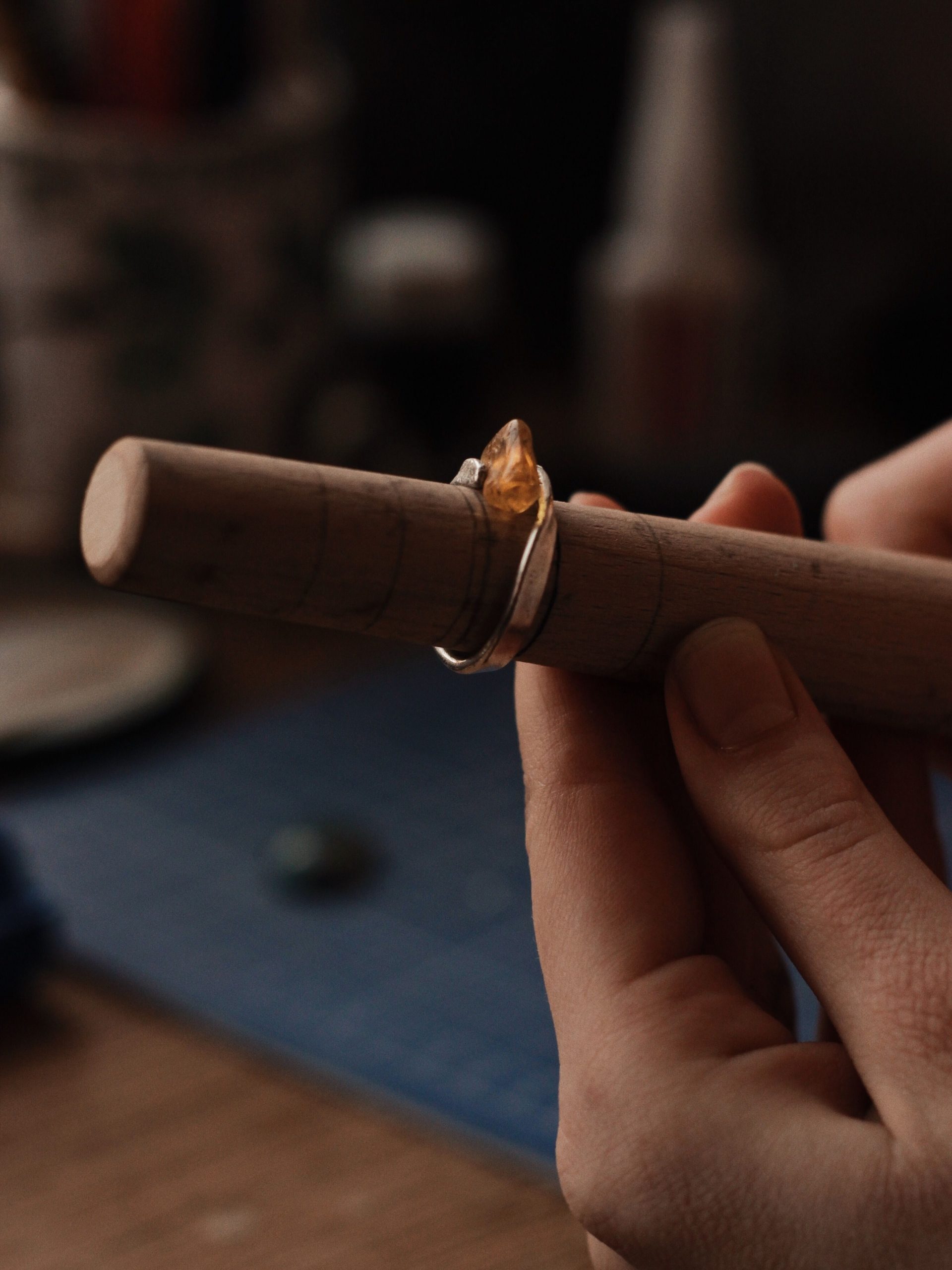 Close-up of hands crafting a gemstone ring on a wooden mandrel. Artisanal craftsmanship in focus.