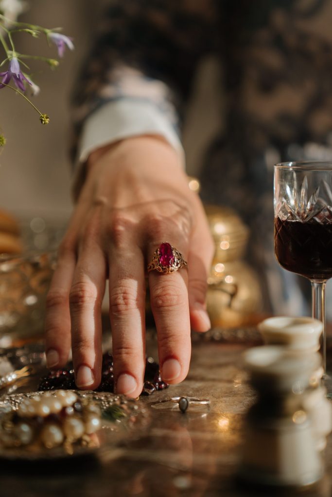 A close-up of an elegant hand adorned with a ruby ring, surrounded by jewelry and a wine glass.